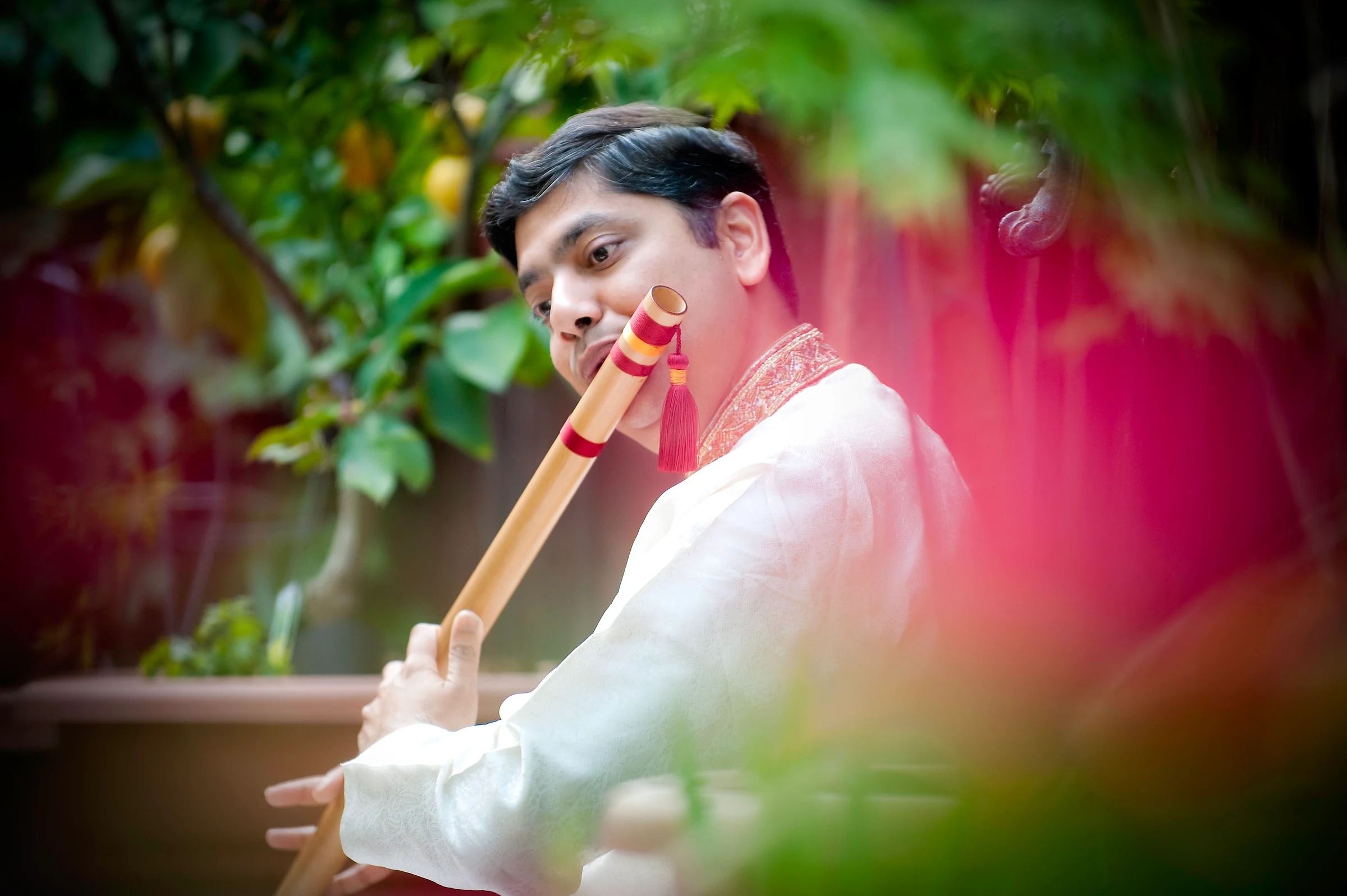 Prasad Bhandarkar playing bansuri behind pink flowers